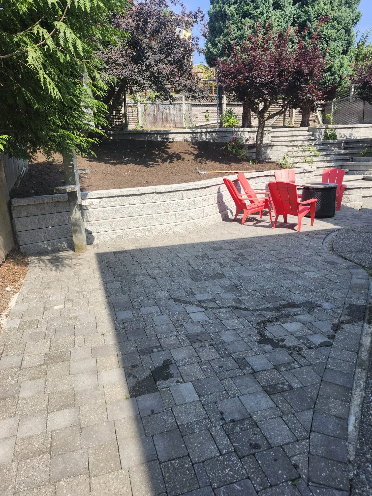 The same paver patio from further back, showing the seat wall, the stepped terrace walls behind it and a freshly mulched bed on the upper level.